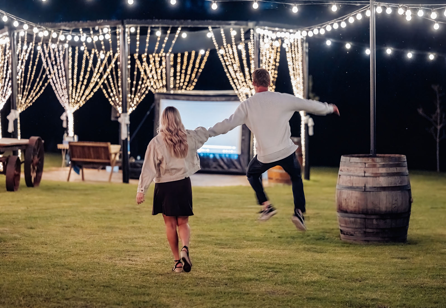 tiny house on the prairie proposal - kyle & bianca 12 Kyle leads Bianca towards a projector screen beneath fairy lights during their Tiny House on the Prairie proposal.