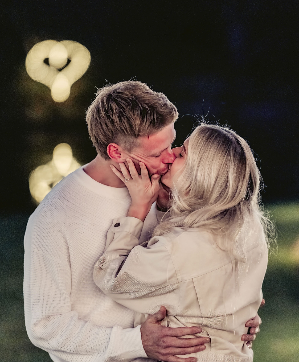 tiny house on the prairie proposal - kyle & bianca 11 Kyle and Bianca kissing outdoors at night, with Bianca’s engagement ring visible and warm fairy lights blurred behind them.