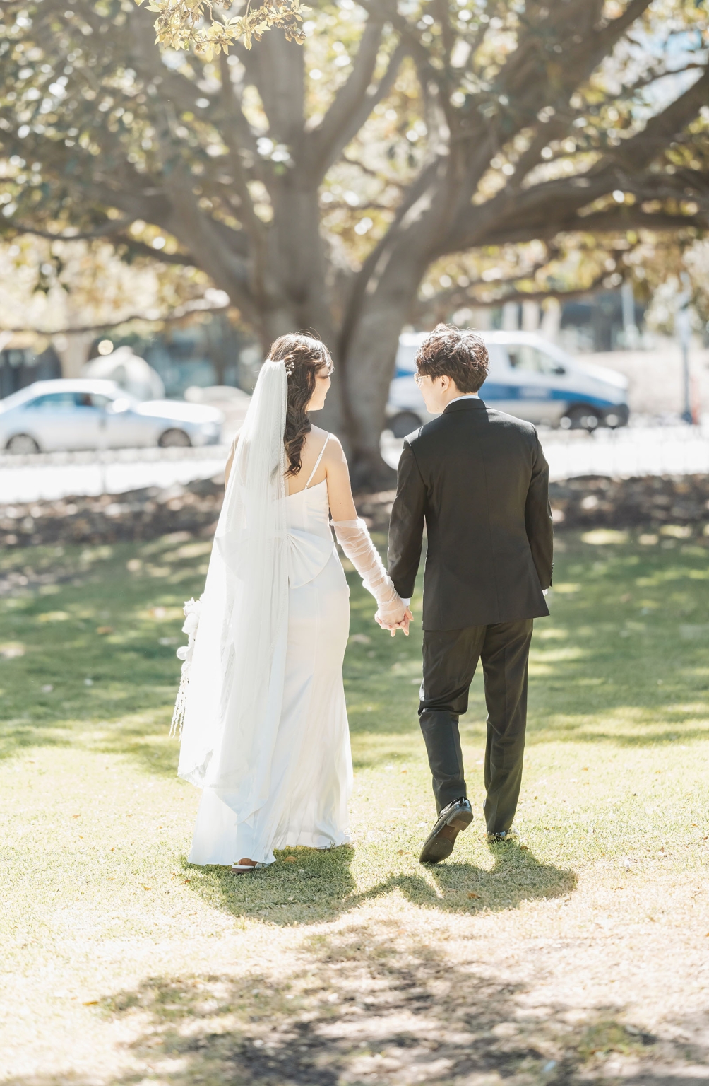 marriage rego office wedding – teri & thomas 23 Teri and Thomas walking hand in hand across a sunlit lawn after their wedding ceremony