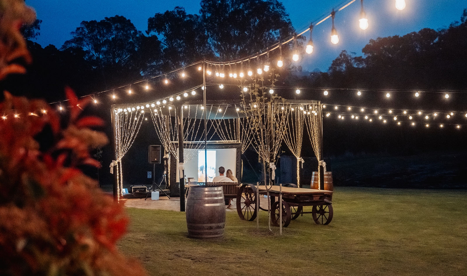 tiny house on the prairie proposal - kyle & bianca 4 Kyle and Bianca sit before a projection screen beneath fairy lights at Tiny House on the Prairie.