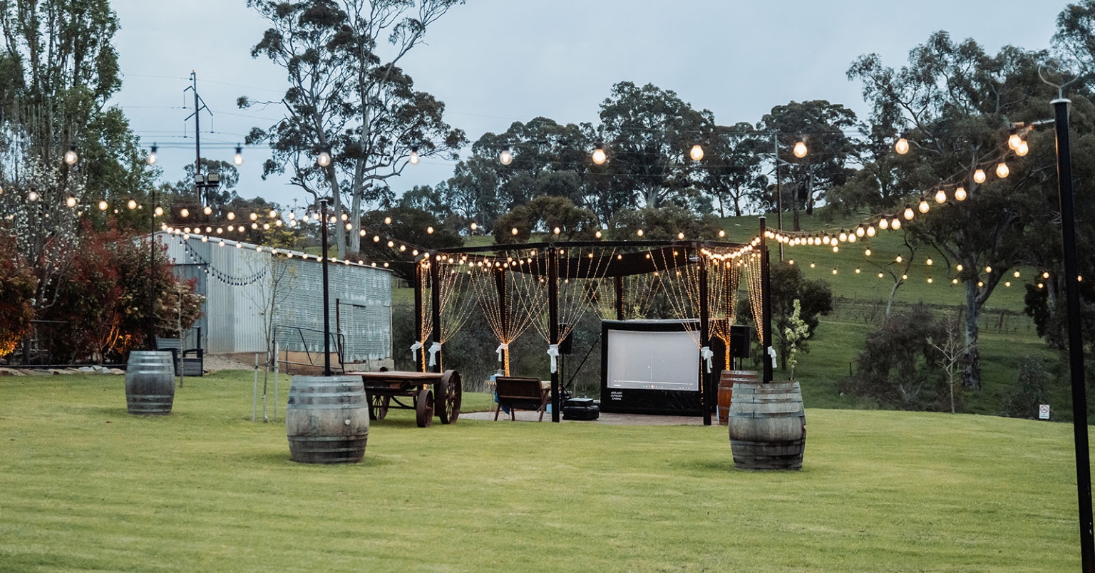 tiny house on the prairie proposal - kyle & bianca 1 Outdoor proposal setup with a projector screen, fairy lights, chairs and wine barrels on a lawn at Tiny House on the Prairie