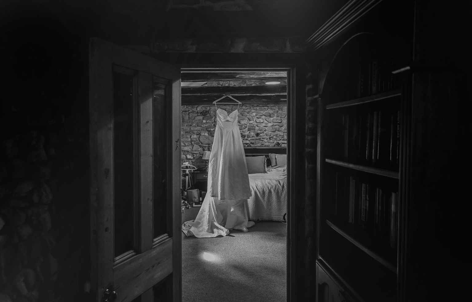 Wedding dress hanging in a rustic stone-walled cottage bedroom