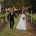 Alysha and Nik walk hand in hand between vineyard rows, with Alysha holding a white bouquet in her wedding dress.