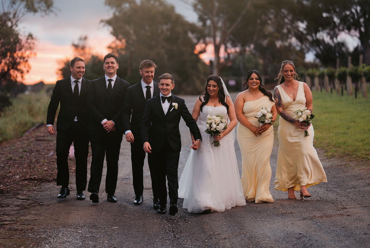 beach road winery wedding – alysha & nik 39 Alysha and Nik walking with their wedding party along a tree-lined road at sunset