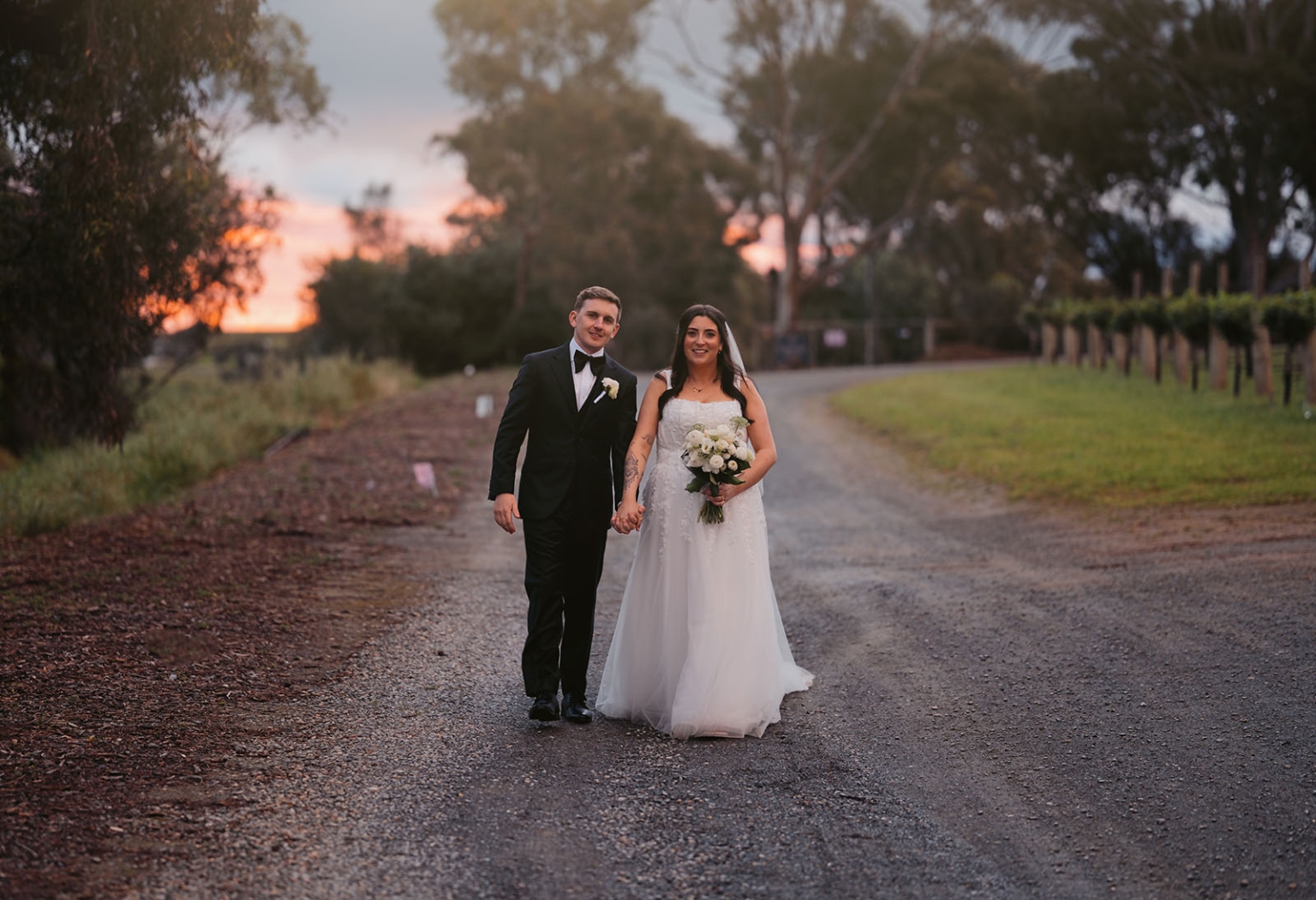 beach road winery wedding – alysha & nik 41 Alysha and Nik walking hand in hand along a tree-lined gravel road at Beach Road Winery at sunset