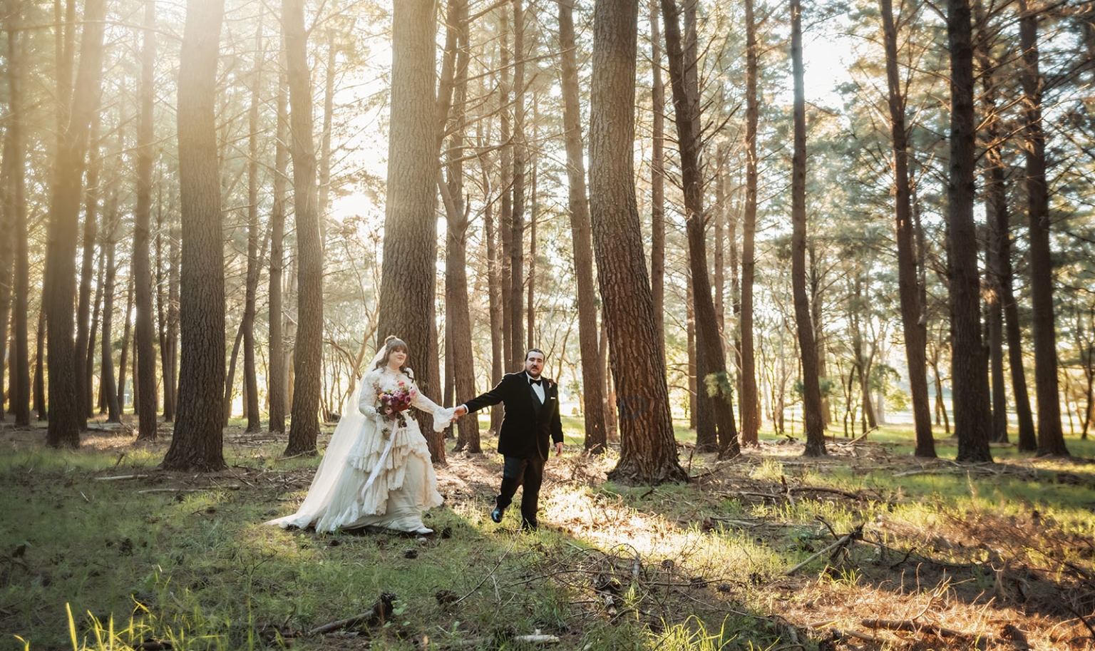 burbrook wedding – amber & angus | kuitpo forest wedding 43 Amber and Angus holding hands among tall pine trees in Kuitpo Forest, with sunlight filtering through the forest.