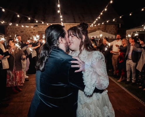 Amber and Angus dancing beneath festoon lights as wedding guests hold sparklers around them