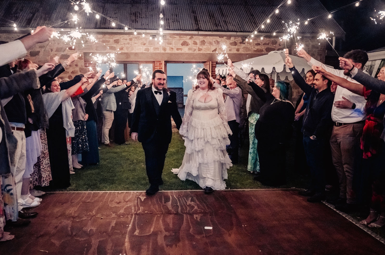 burbrook wedding – amber & angus | kuitpo forest wedding 60 Amber and Angus walk through guests holding sparklers beneath festoon lights at their Burbrook wedding.