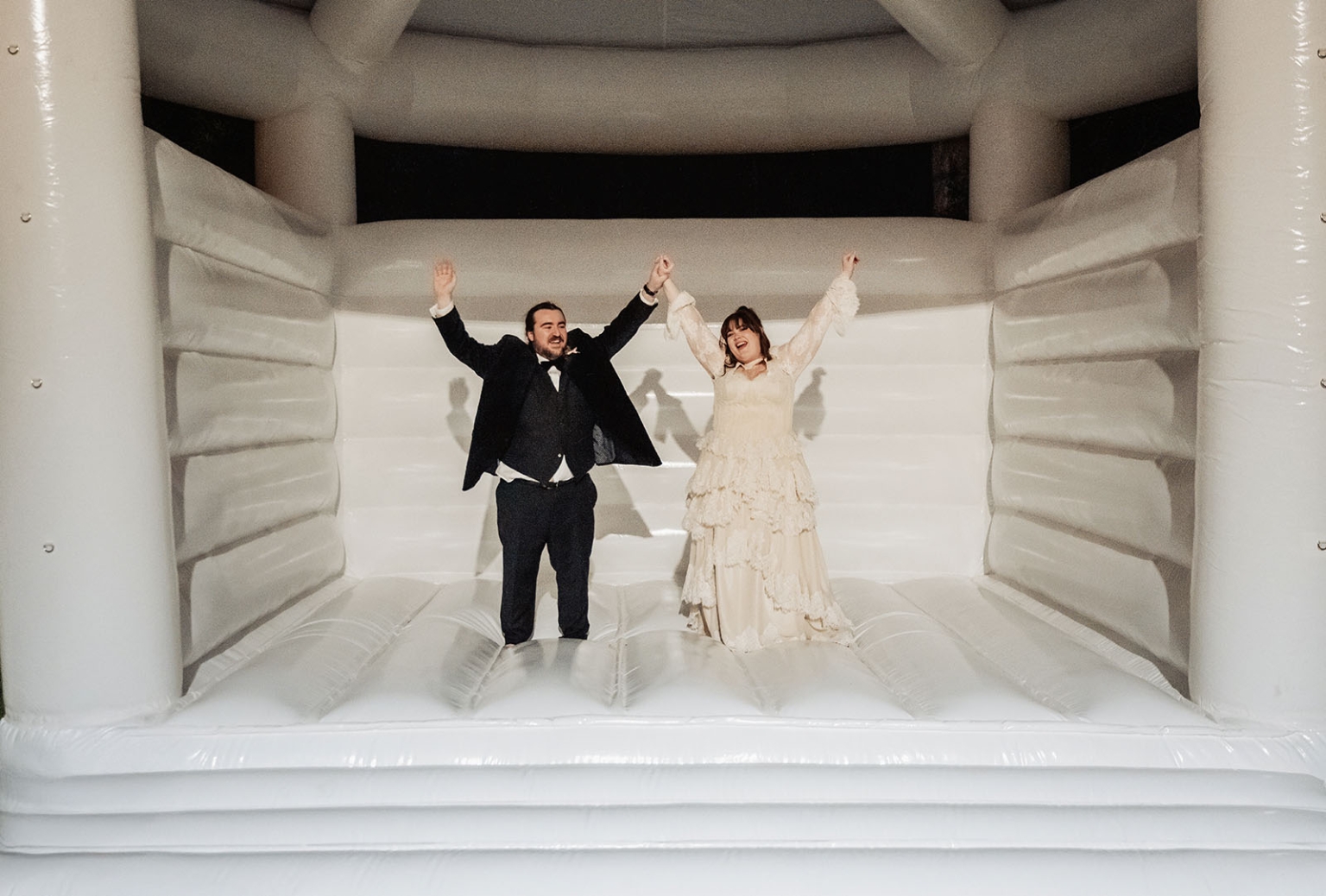burbrook wedding – amber & angus | kuitpo forest wedding 57 Amber and Angus raise their joined hands while standing inside a white wedding bouncy castle.