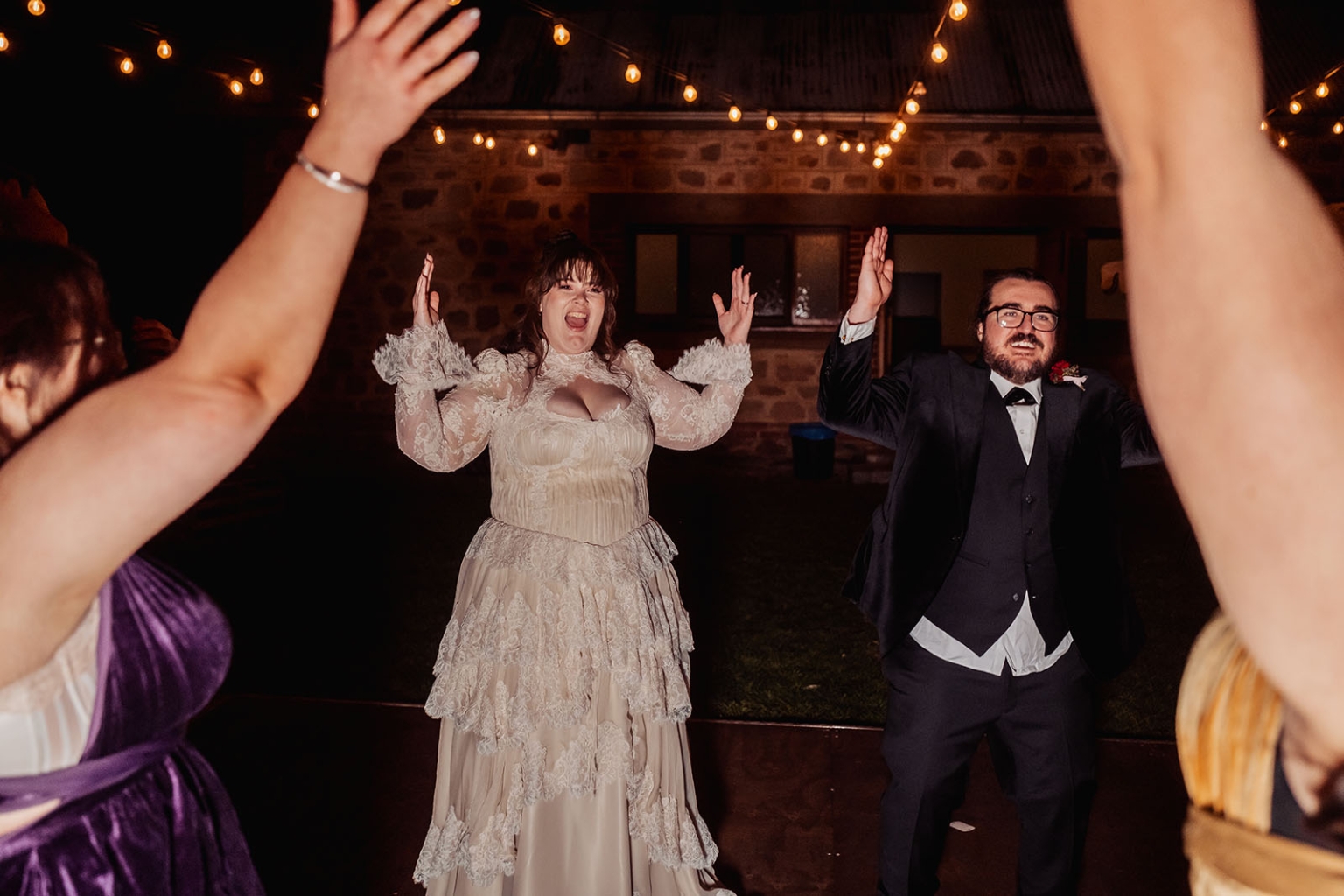 burbrook wedding – amber & angus | kuitpo forest wedding 65 Amber and Angus dance with raised hands among guests beneath festoon lights at their wedding reception.