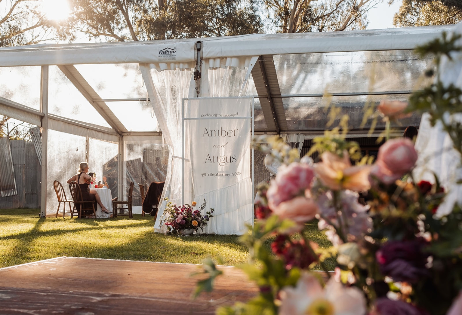 burbrook wedding – amber & angus | kuitpo forest wedding 52 Wedding reception marquee with a sign for Amber and Angus, seated guests and colourful flowers in the foreground