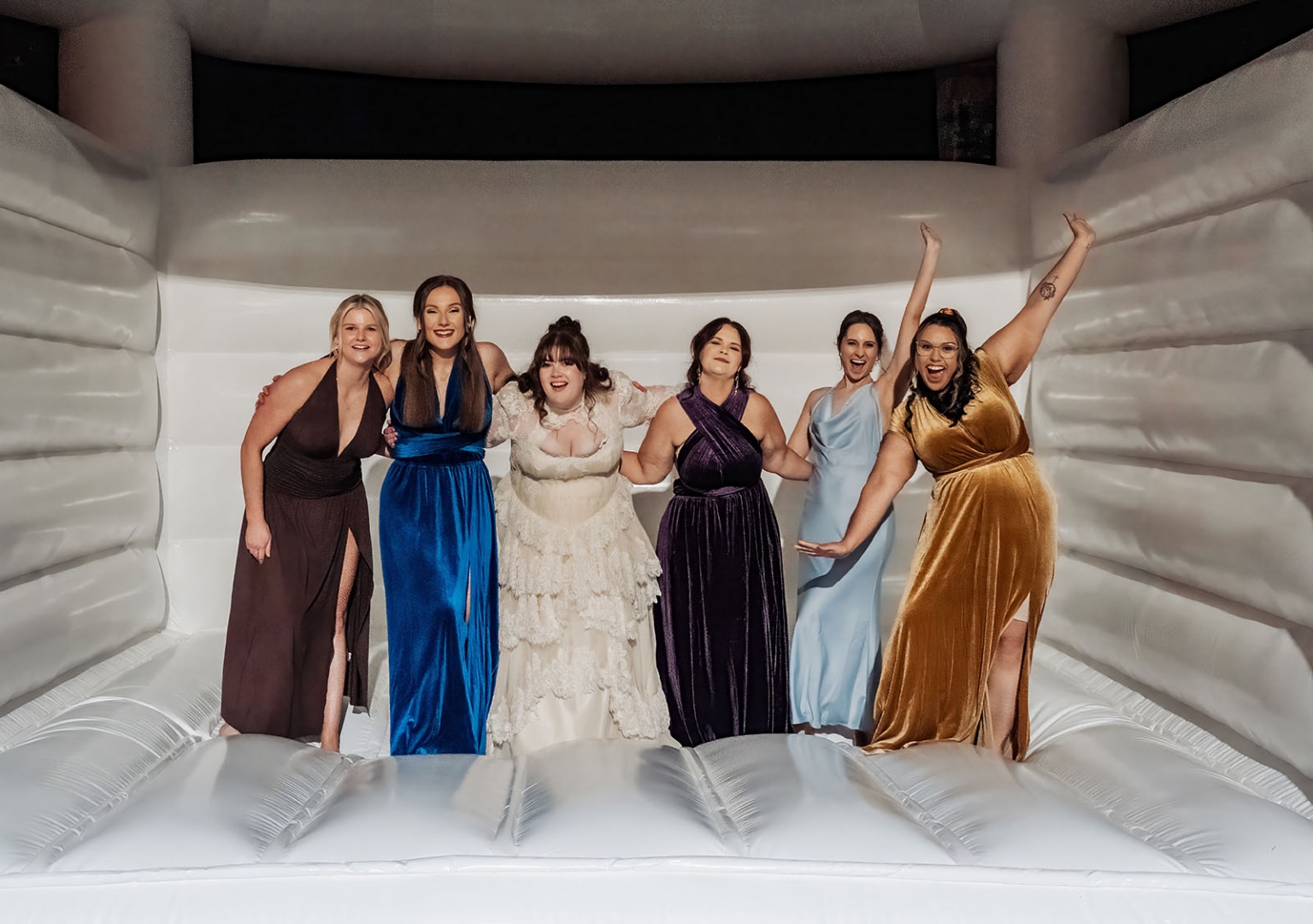 burbrook wedding – amber & angus | kuitpo forest wedding 58 Bride Amber and five bridesmaids in colourful formal dresses standing inside a white inflatable bouncy castle at the wedding.