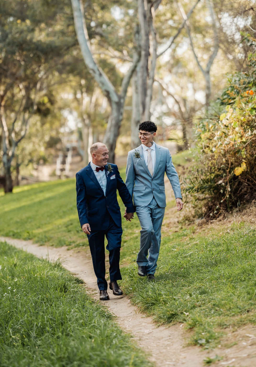 hotel royal wedding - brad & manuel 14 Brad and Manuel in wedding suits walking hand in hand along a leafy park path