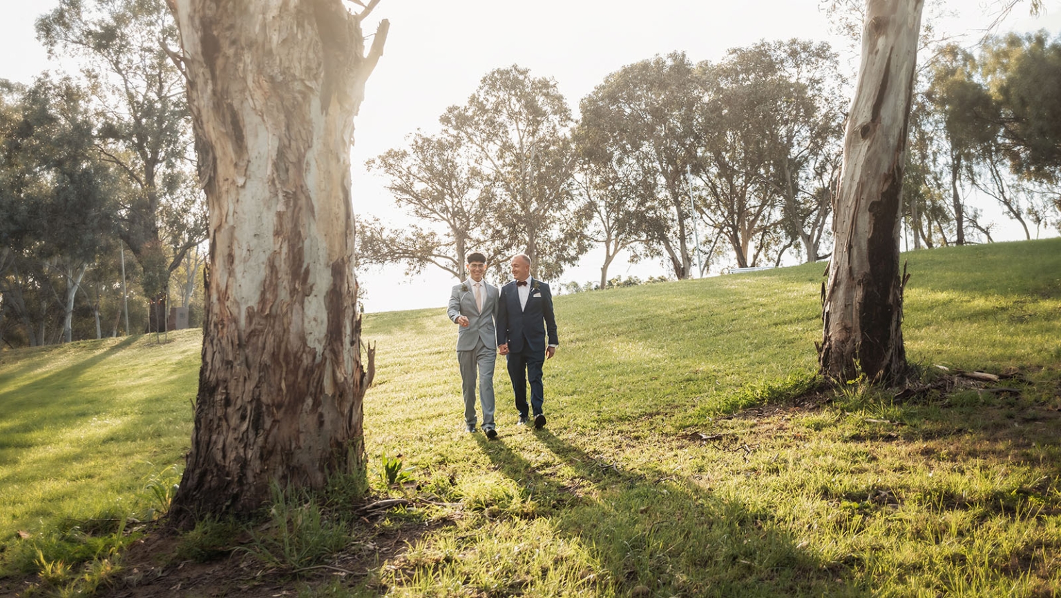 hotel royal wedding - brad & manuel 16 Brad and Manuel in suits walking hand in hand through a sunlit park between eucalyptus trees