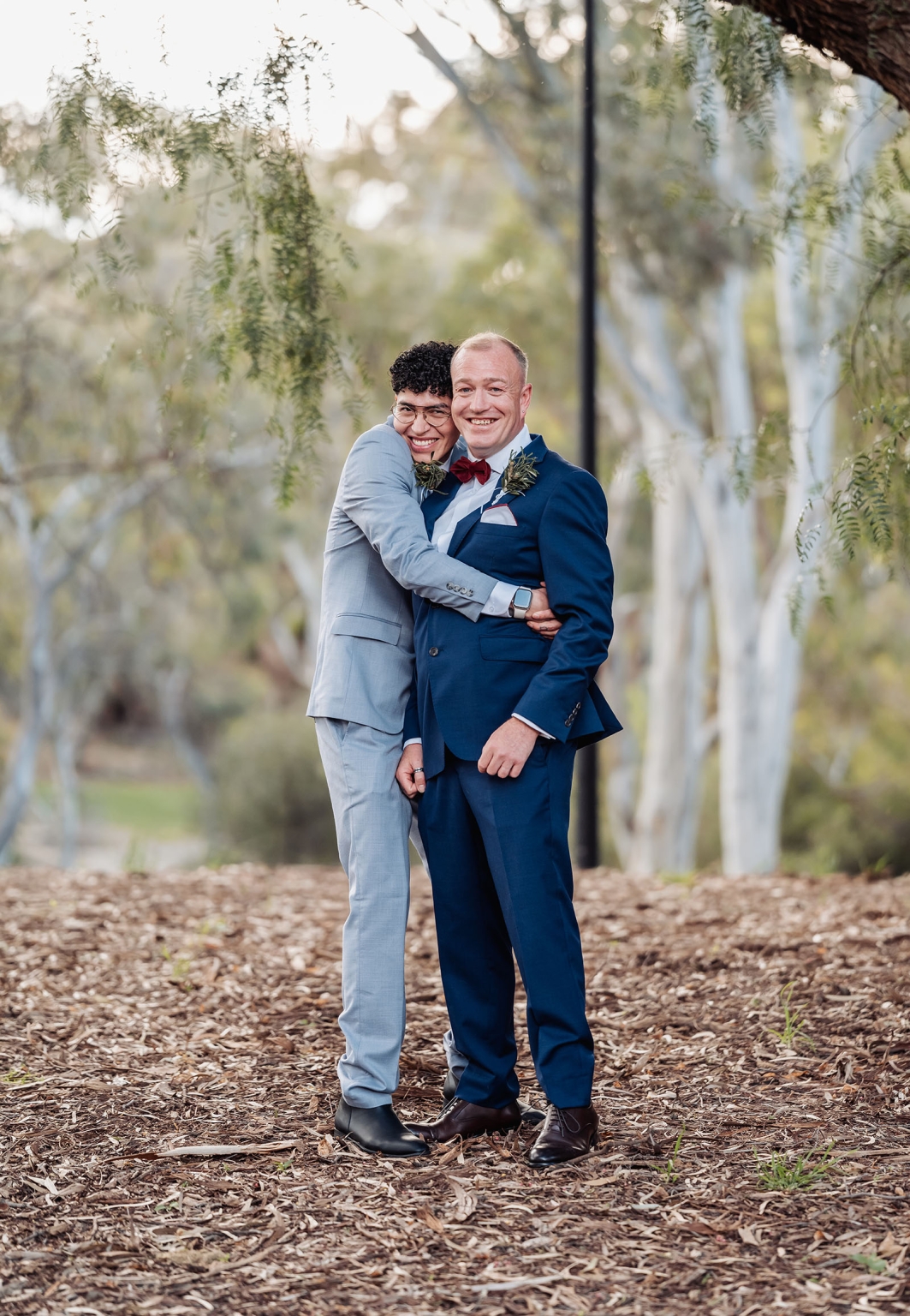hotel royal wedding - brad & manuel 10 Brad and Manuel smiling and embracing in suits beneath leafy trees during their wedding portrait session