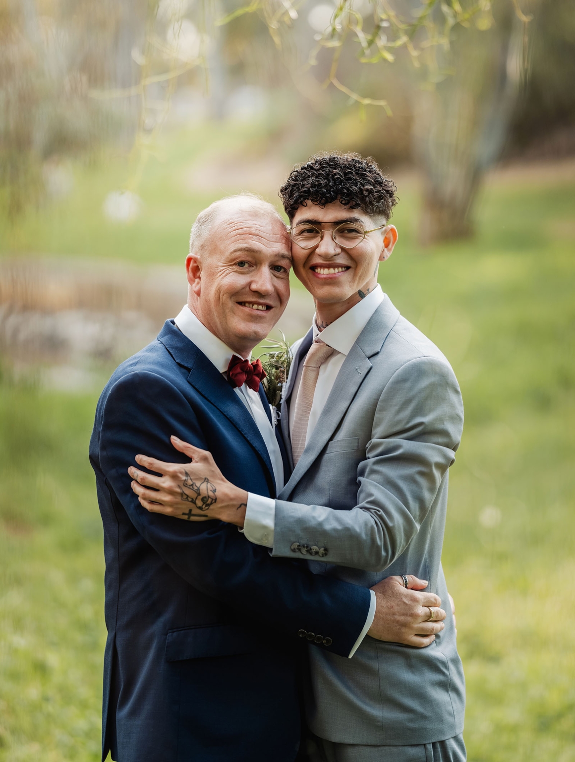 hotel royal wedding - brad & manuel 20 Brad and Manuel smiling as they embrace in suits during their wedding portrait session in a leafy park