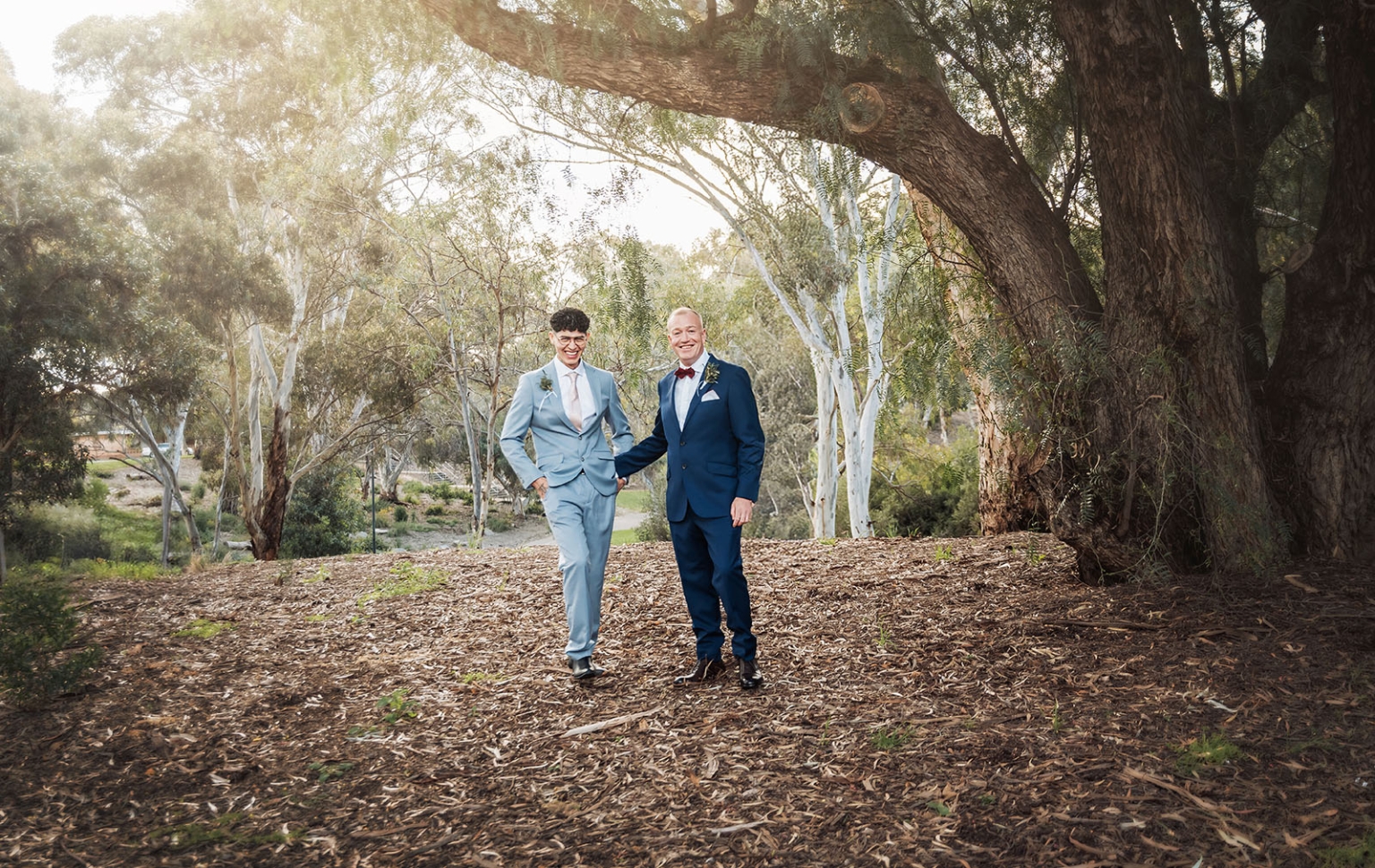 hotel royal wedding - brad & manuel 9 Brad and Manuel standing together in tailored suits beneath a large eucalyptus tree in a leafy park