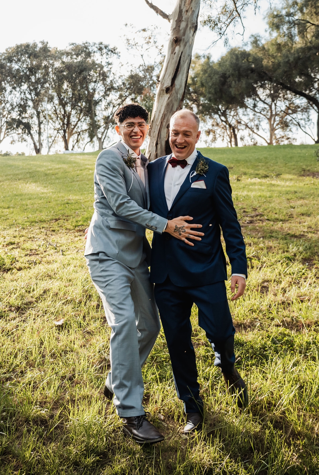 hotel royal wedding - brad & manuel 17 Brad and Manuel laughing together in suits on grass beneath eucalyptus trees during their wedding portraits