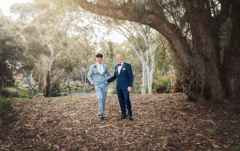 hotel royal wedding - brad & manuel 1 Brad and Manuel standing together in tailored suits beneath a large eucalyptus tree in a leafy park