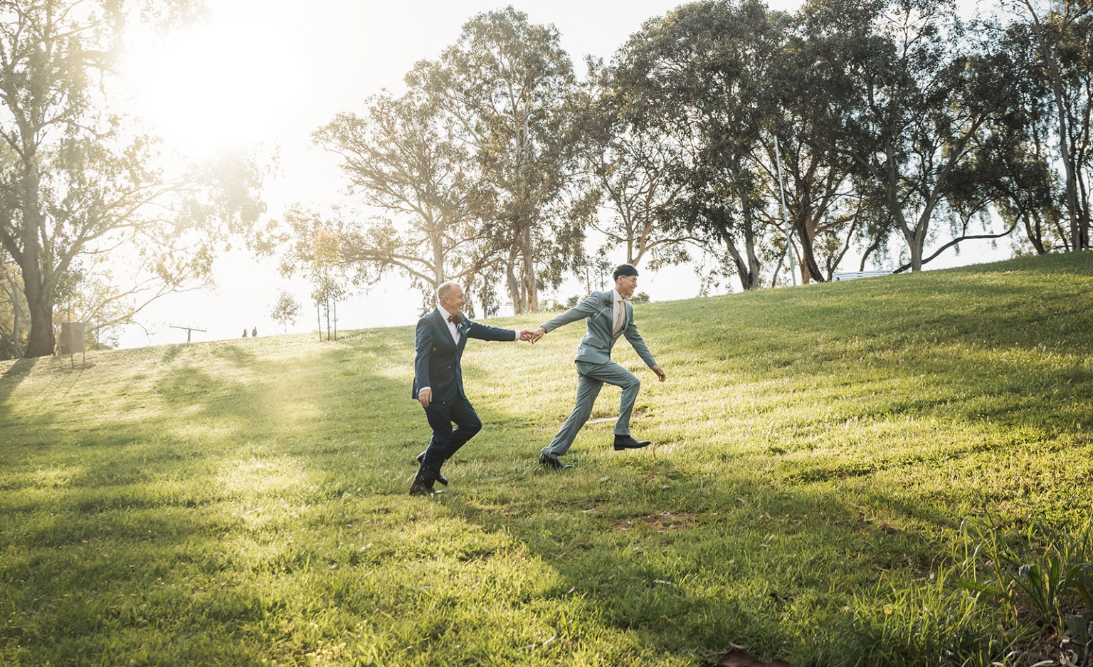 hotel royal wedding - brad & manuel 15 Brad and Manuel holding hands as they run up a sunlit grassy hill beneath tall trees