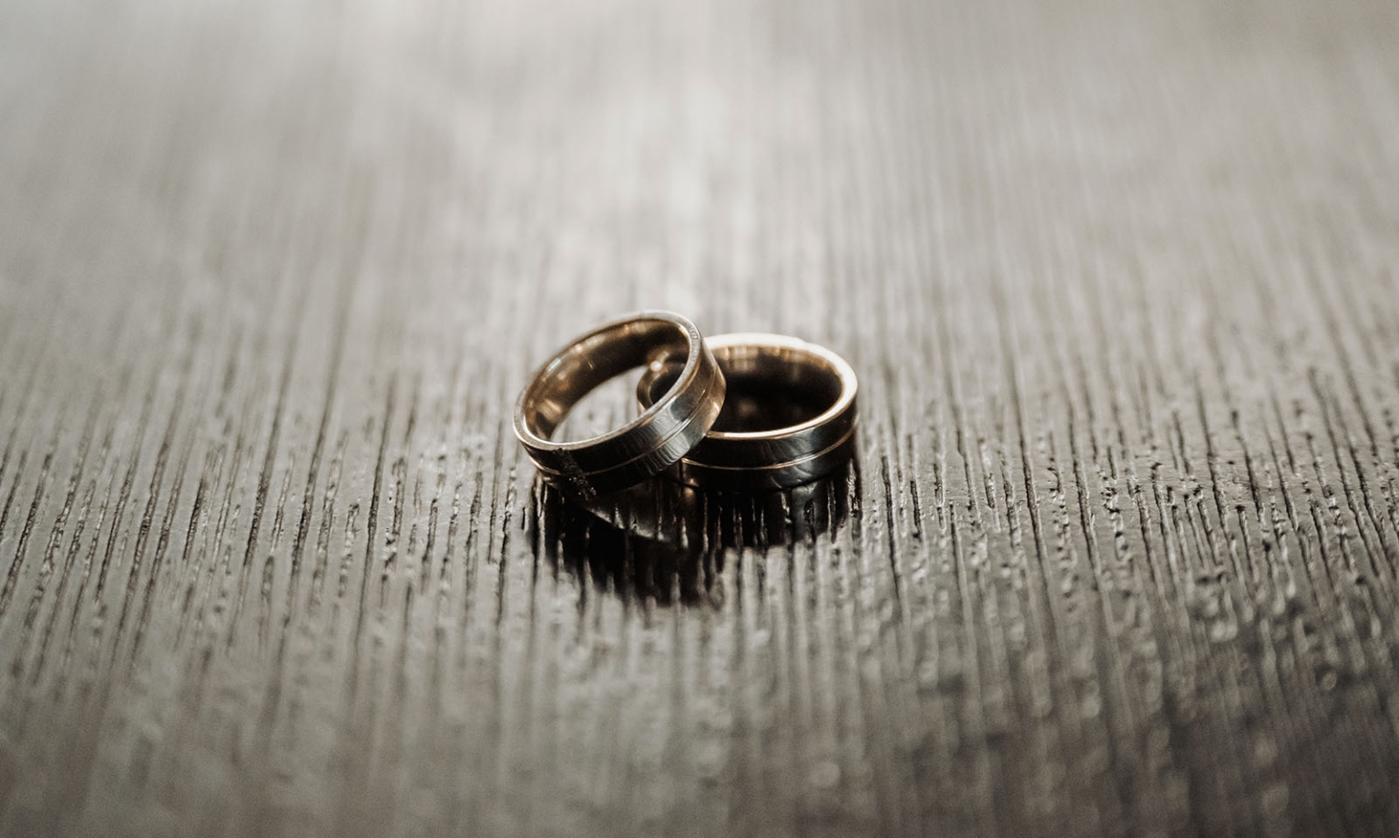hotel royal wedding - brad & manuel 2 Two dark metal wedding bands resting together on a textured wooden surface