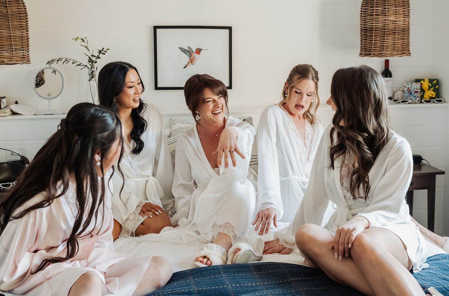 serafino winery wedding – maor & sasha 16 Five women in white satin robes laughing together on a bed during wedding preparations