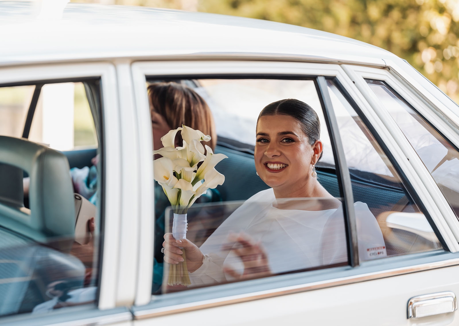st joseph's chapel wedding – diana & michael 5 Bride smiling from the back seat of a white car while holding a bouquet of white calla lilies