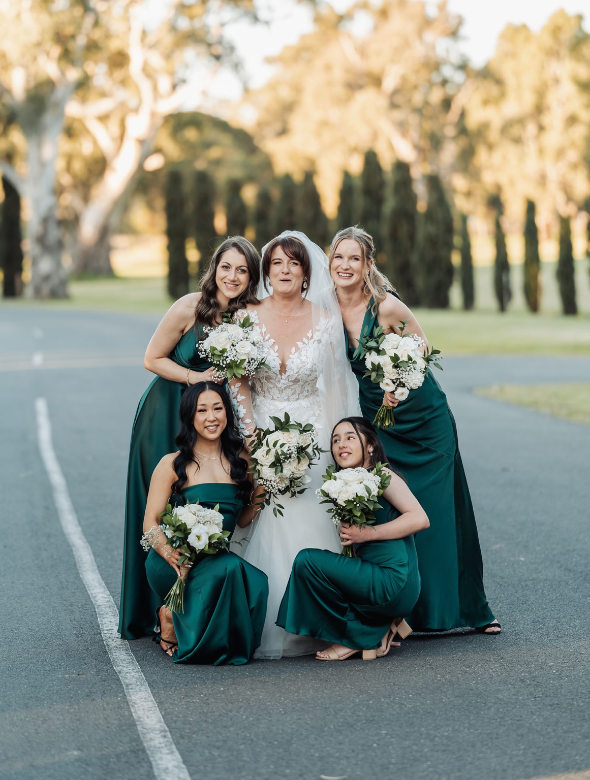 serafino winery wedding – maor & sasha 45 Bride in a lace wedding gown with four bridesmaids in deep green dresses holding white flower bouquets at Serafino Winery
