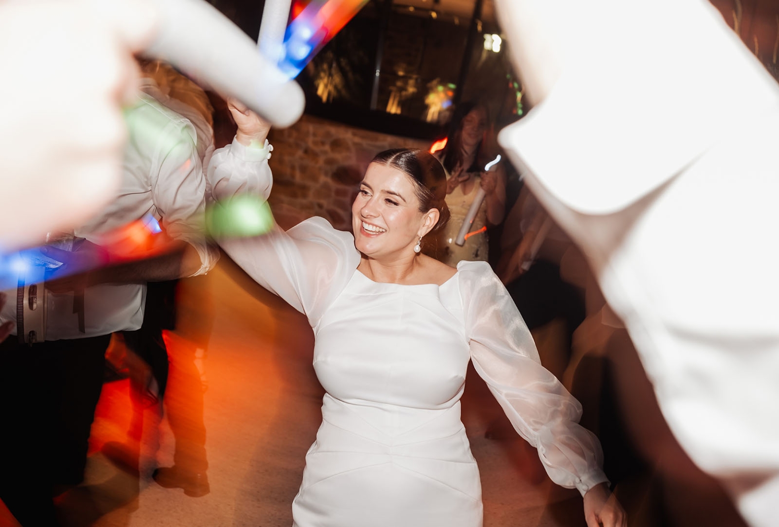 st joseph's chapel wedding – diana & michael 56 Bride in a white wedding dress dancing with guests under colourful lights at the reception
