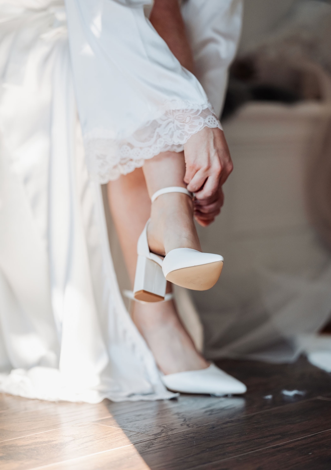 serafino winery wedding – maor & sasha 18 Bride in a lace-trimmed white robe fastening the ankle strap of a white block-heeled wedding shoe