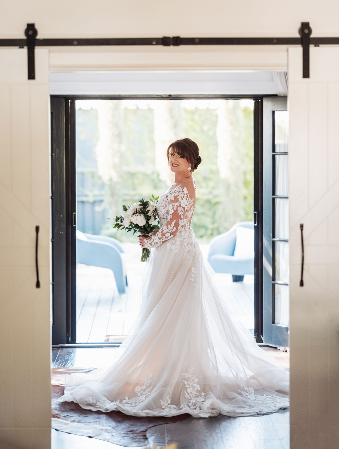 serafino winery wedding – maor & sasha 21 Bride in a long-sleeved lace wedding gown holding a white and green bouquet in an open doorway