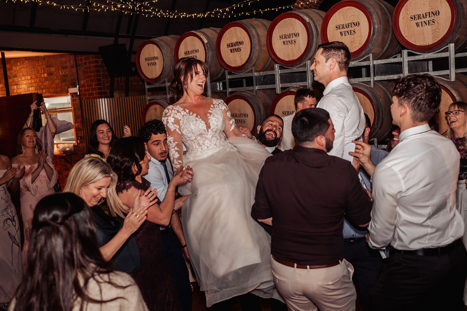 serafino winery wedding – maor & sasha 68 Bride laughing as wedding guests lift her on the dance floor beneath Serafino Wines barrels
