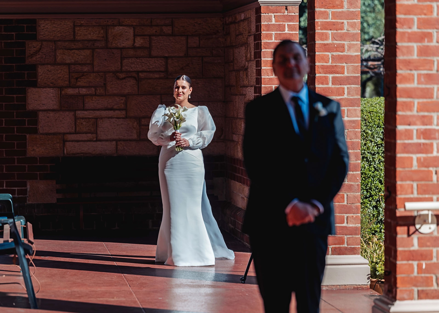 st joseph's chapel wedding – diana & michael 6 Bride holding a white bouquet waits at the chapel entrance while the groom stands out of focus in the foreground.