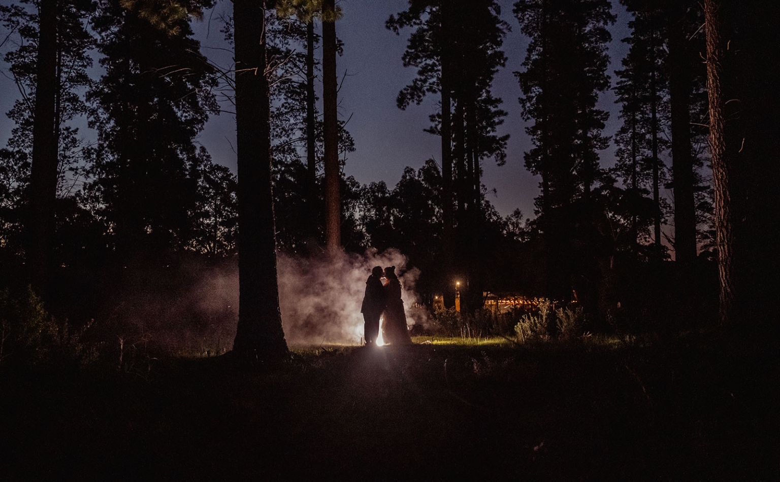 burbrook wedding – amber & angus | kuitpo forest wedding 66 Newlyweds embracing in silhouette among tall trees, backlit by mist at night in Burbrook Forest.