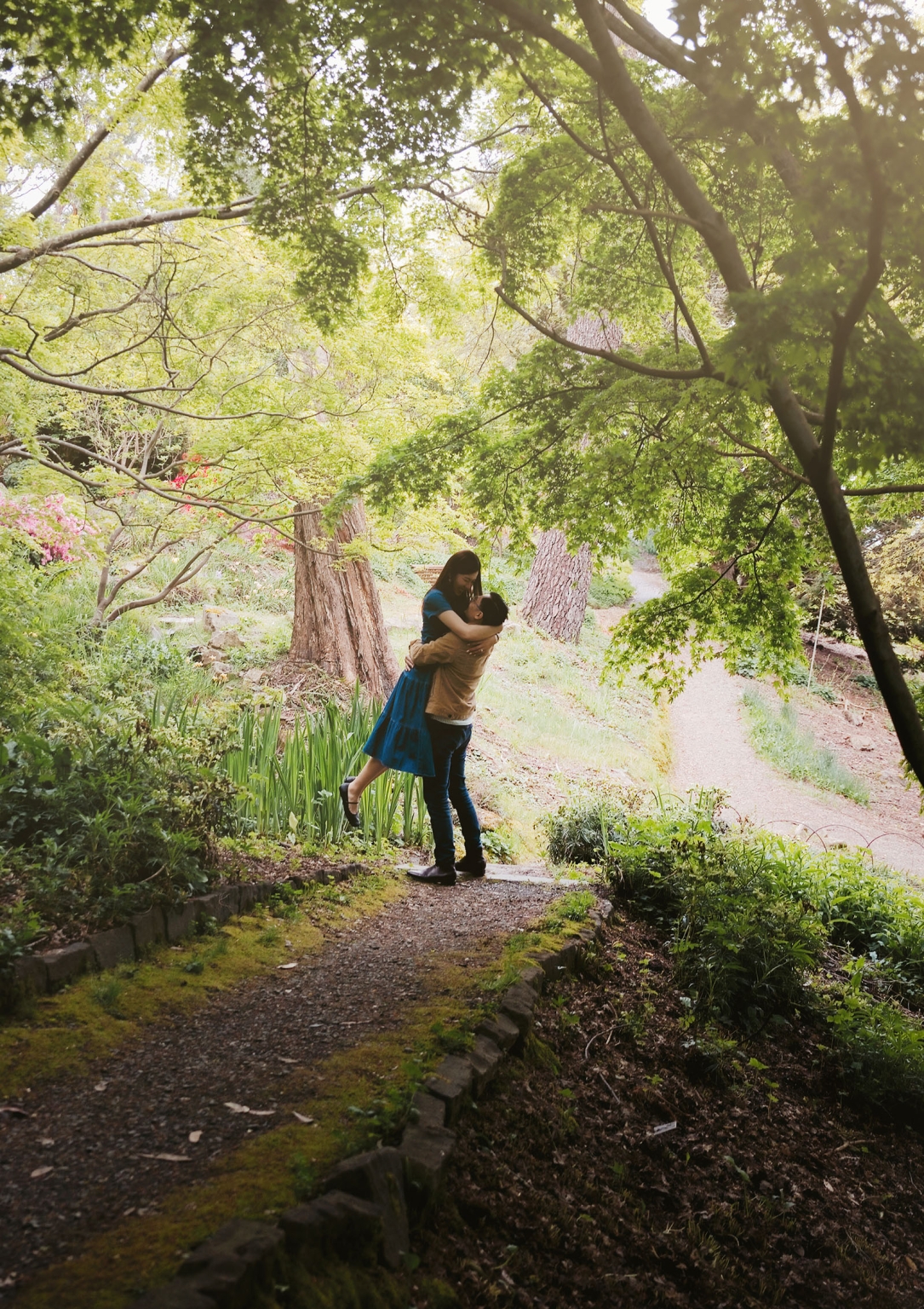mt lofty botanic park proposal – watay & phouthun 19 Couple embracing beneath leafy trees beside a garden path at Mount Lofty Botanic Garden