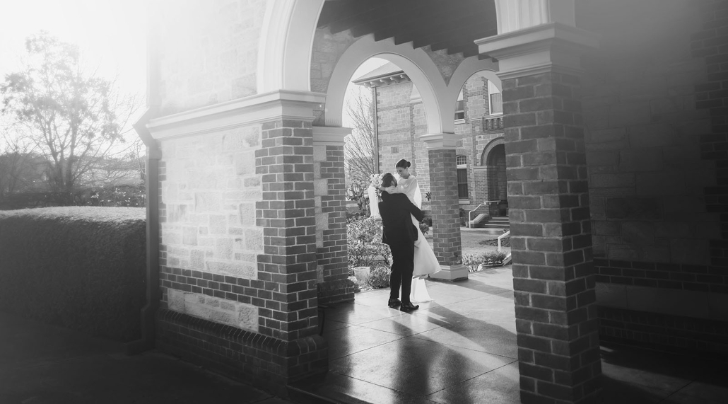 Bride and groom embracing beneath the arched brick portico at St Joseph's Chapel in Kensington