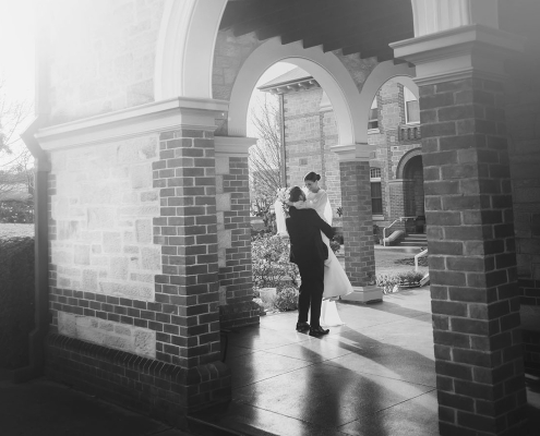 Bride and groom embracing beneath the arched brick portico at St Joseph's Chapel in Kensington