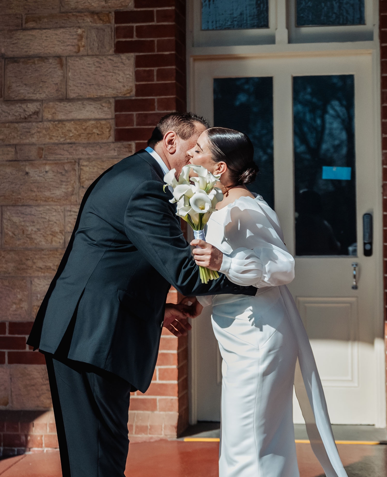 st joseph's chapel wedding – diana & michael 8 Diana and Michael kissing outside St Joseph's Chapel, with Diana holding a bouquet of white calla lilies.