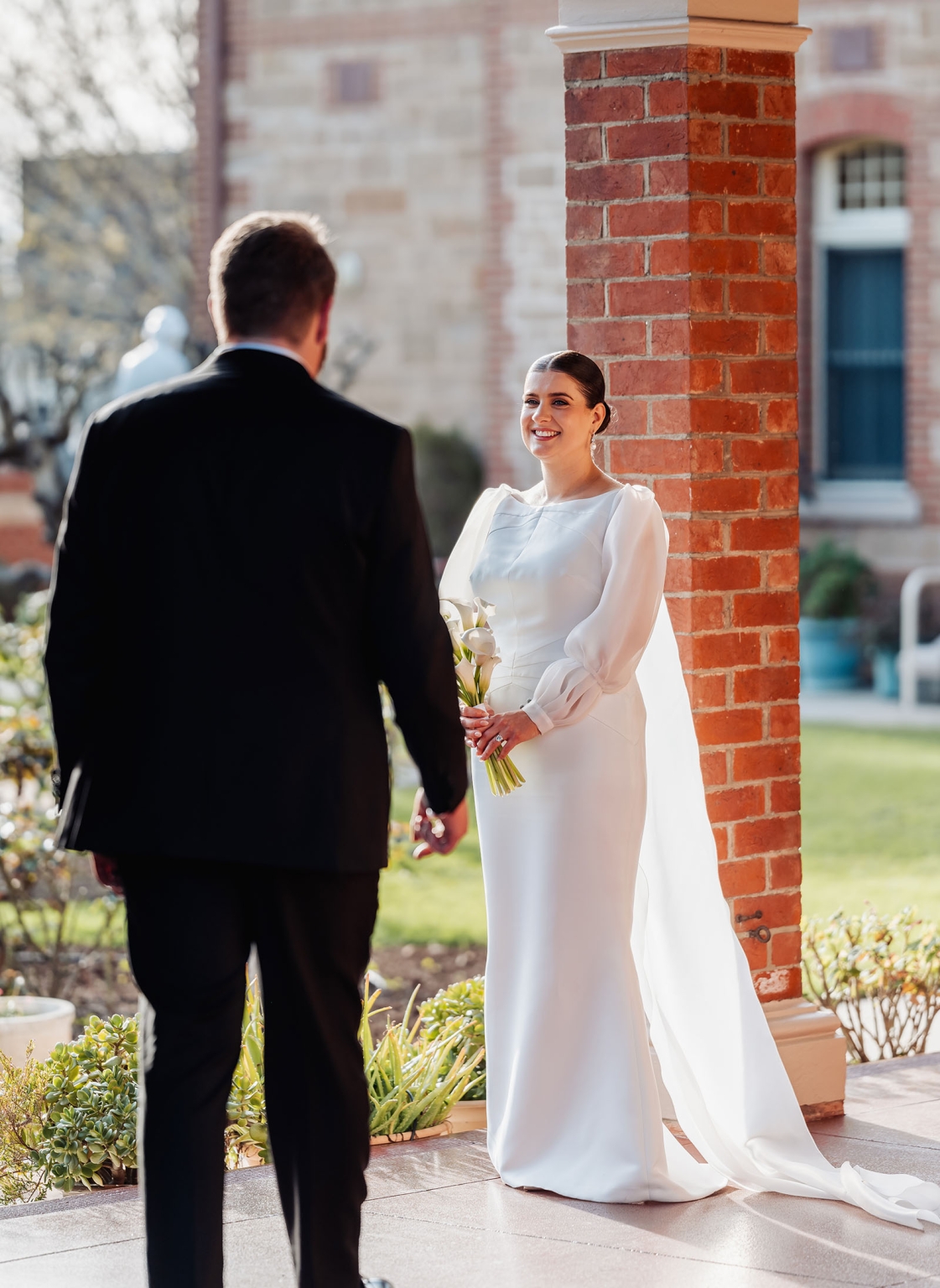 st joseph's chapel wedding – diana & michael 22 Bride holding a white calla lily bouquet smiles at the groom during their first look beside a red brick chapel column.