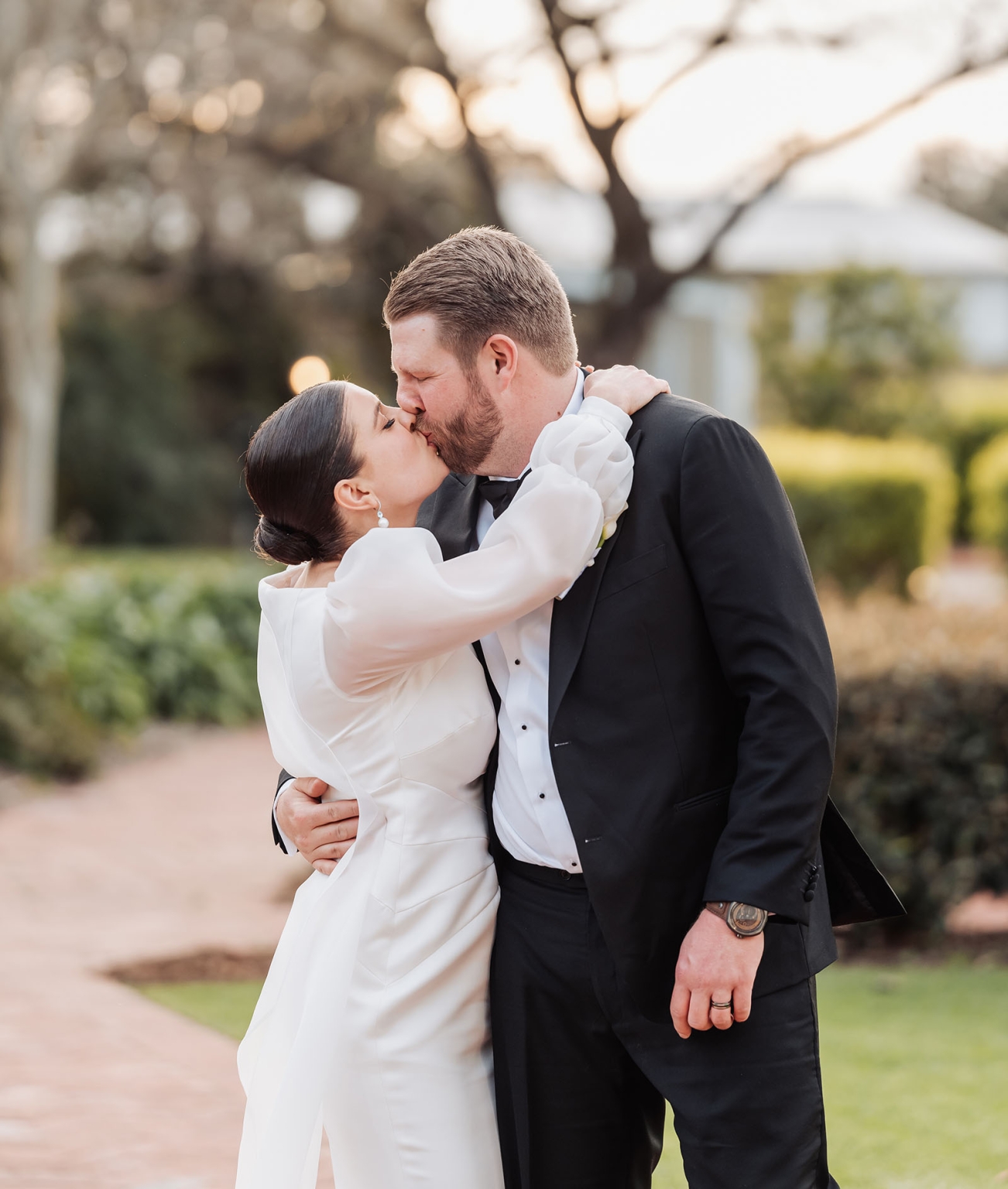 st joseph's chapel wedding – diana & michael 34 Diana and Michael kissing in a sunlit garden, wearing a white wedding dress and black tuxedo