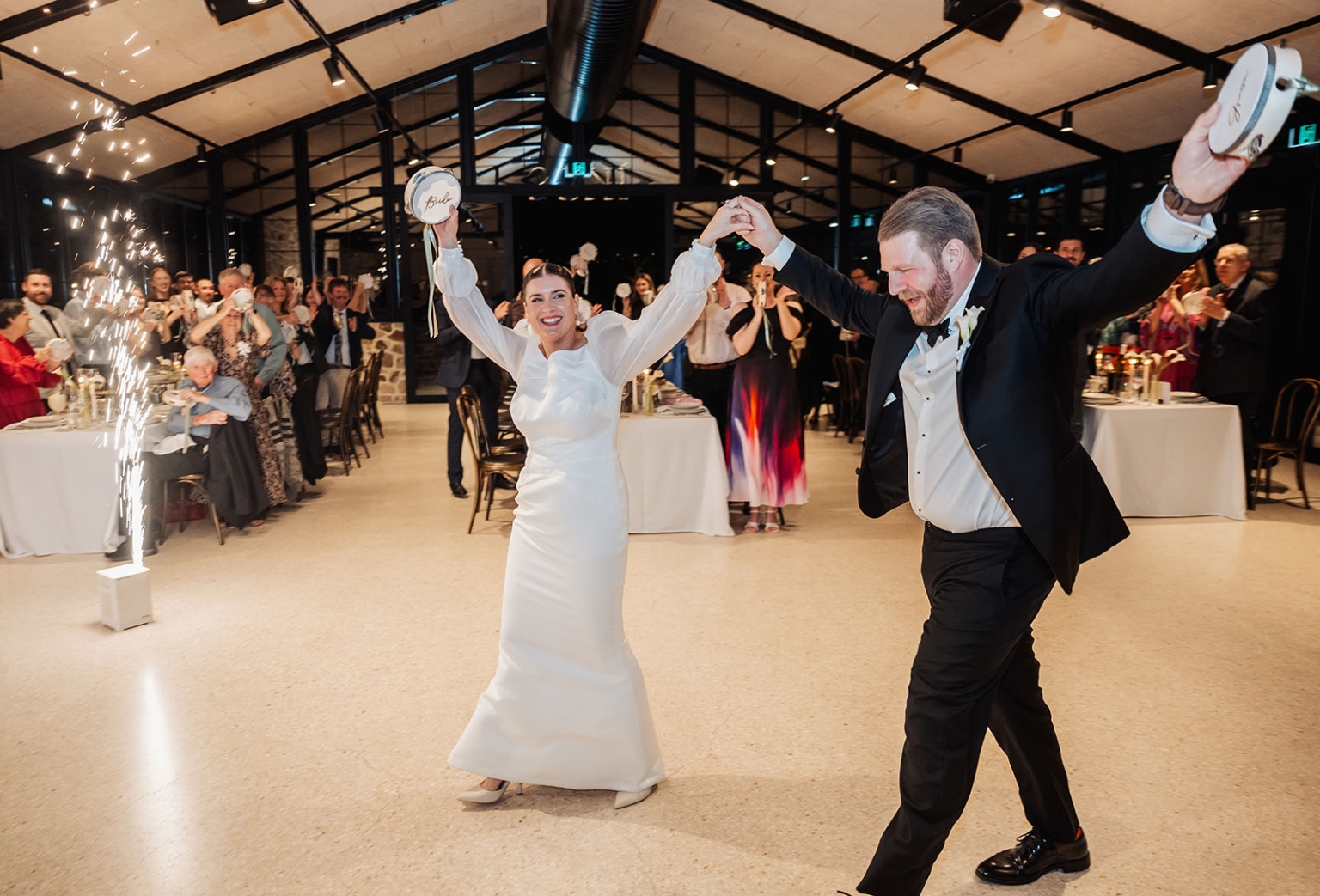 st joseph's chapel wedding – diana & michael 45 Diana and Michael enter their wedding reception holding tambourines as guests cheer beside an indoor sparkler fountain.