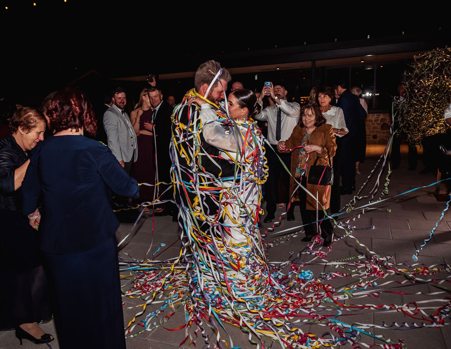 st joseph's chapel wedding – diana & michael 60 Diana and Michael embrace as wedding guests wrap them in colourful streamers during a nighttime send-off.