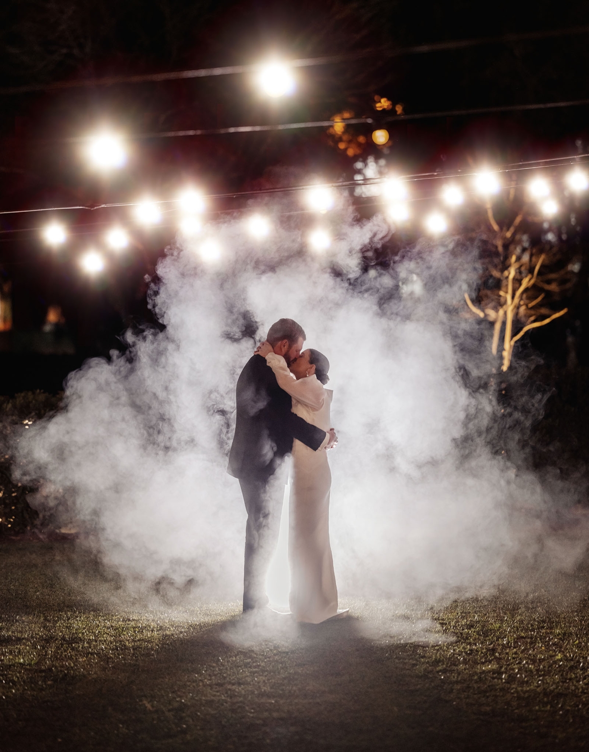 st joseph's chapel wedding – diana & michael 47 Diana and Michael kissing beneath festoon lights, surrounded by smoke during their wedding reception.