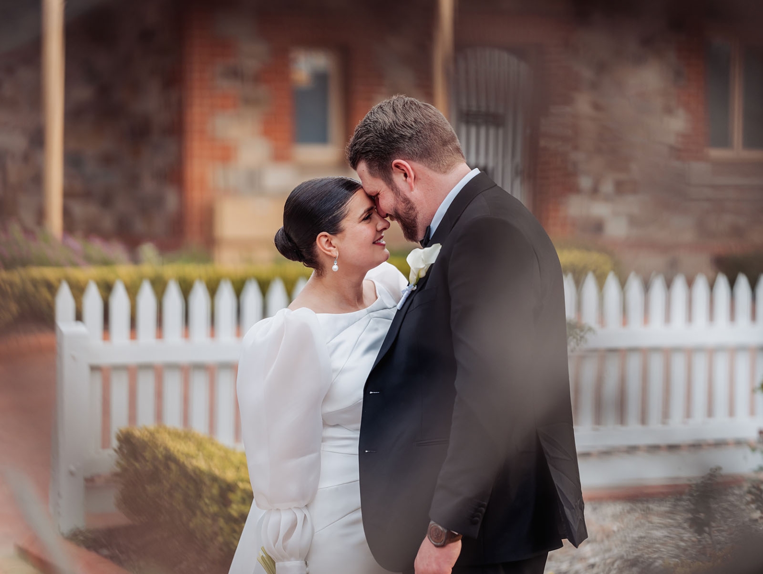 st joseph's chapel wedding – diana & michael 35 Diana and Michael touch foreheads outside St Joseph's Chapel, with a white picket fence behind them.