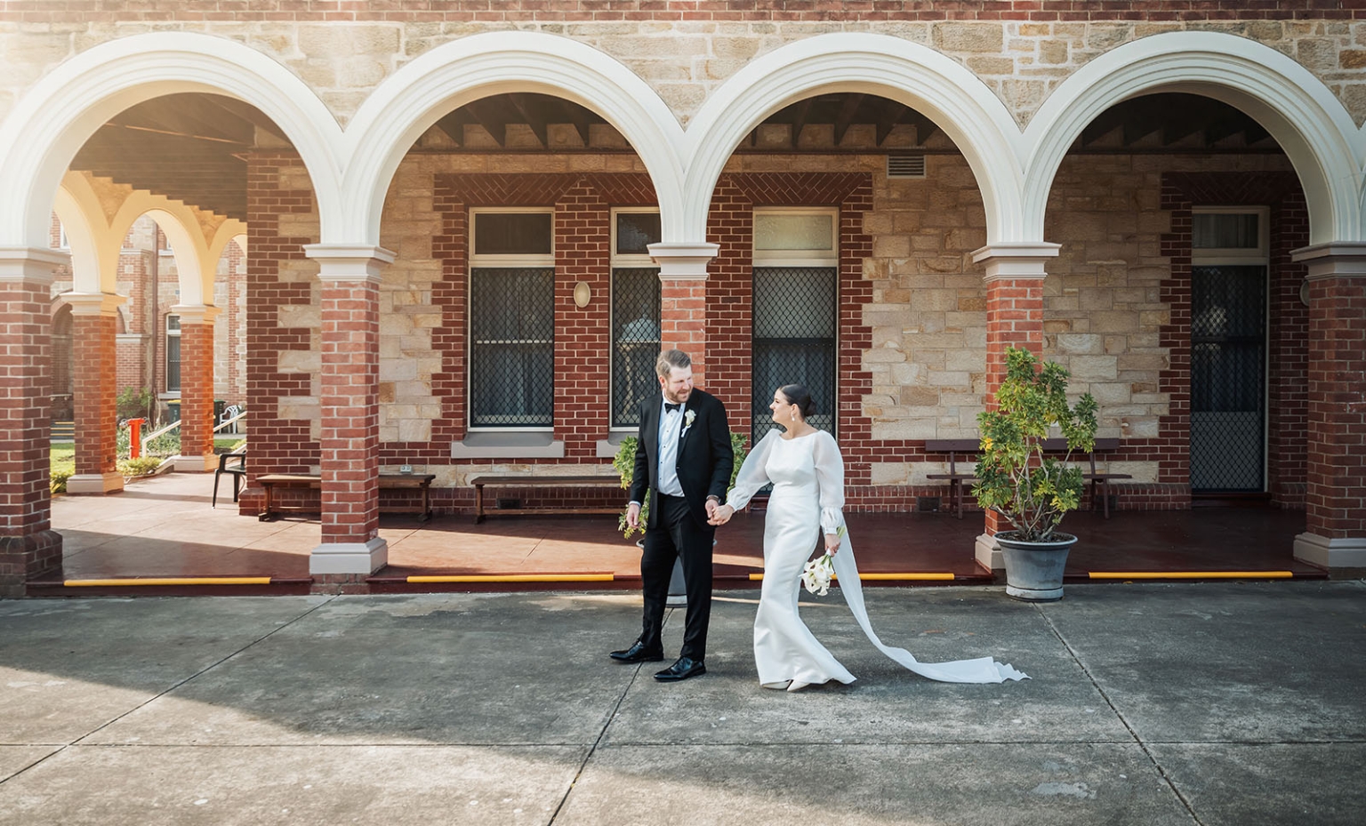 st joseph's chapel wedding – diana & michael 21 Diana and Michael holding hands outside St Joseph's Chapel, with arched brick colonnades behind them.