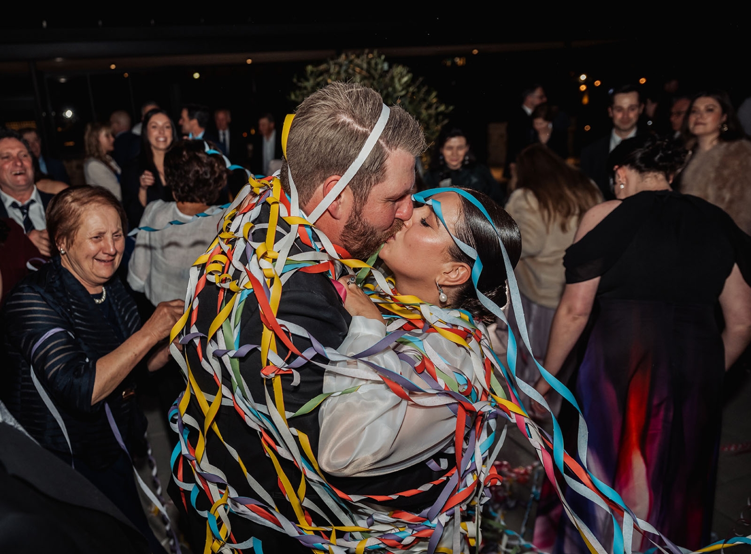 st joseph's chapel wedding – diana & michael 59 Diana and Michael kissing on the dance floor, wrapped in colourful streamers as wedding guests celebrate around them