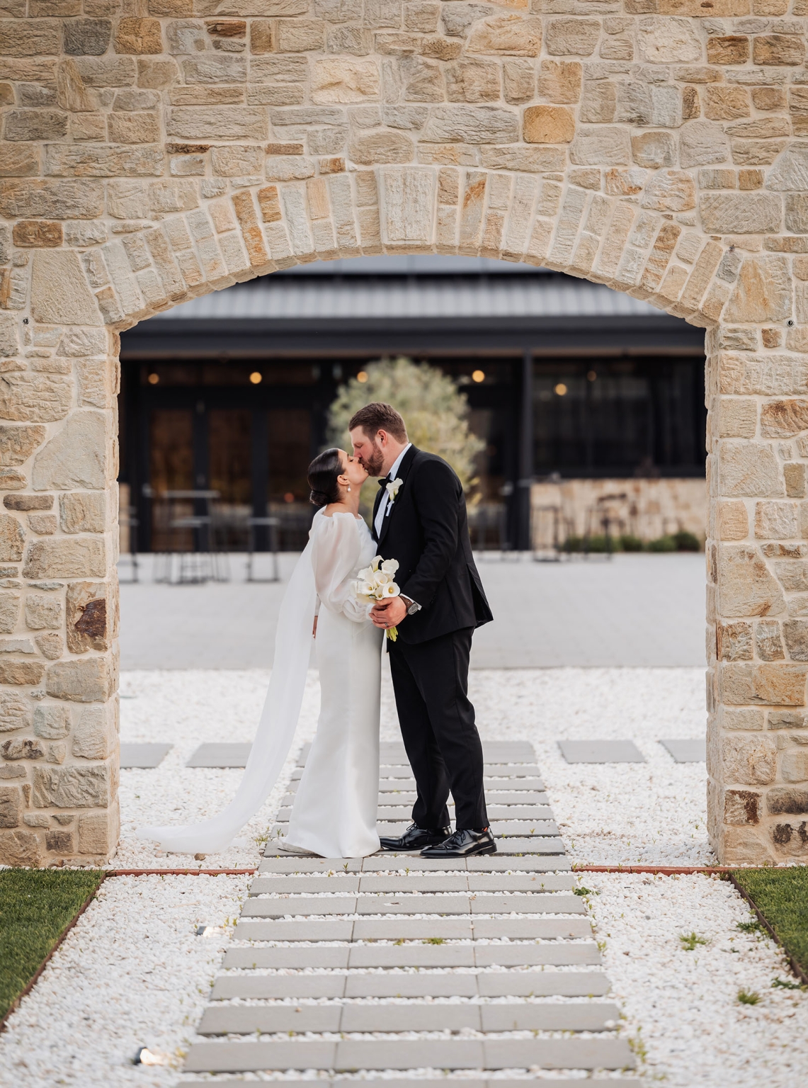 st joseph's chapel wedding – diana & michael 40 Diana and Michael kissing beneath a sandstone arch, with Diana holding a white orchid bouquet.