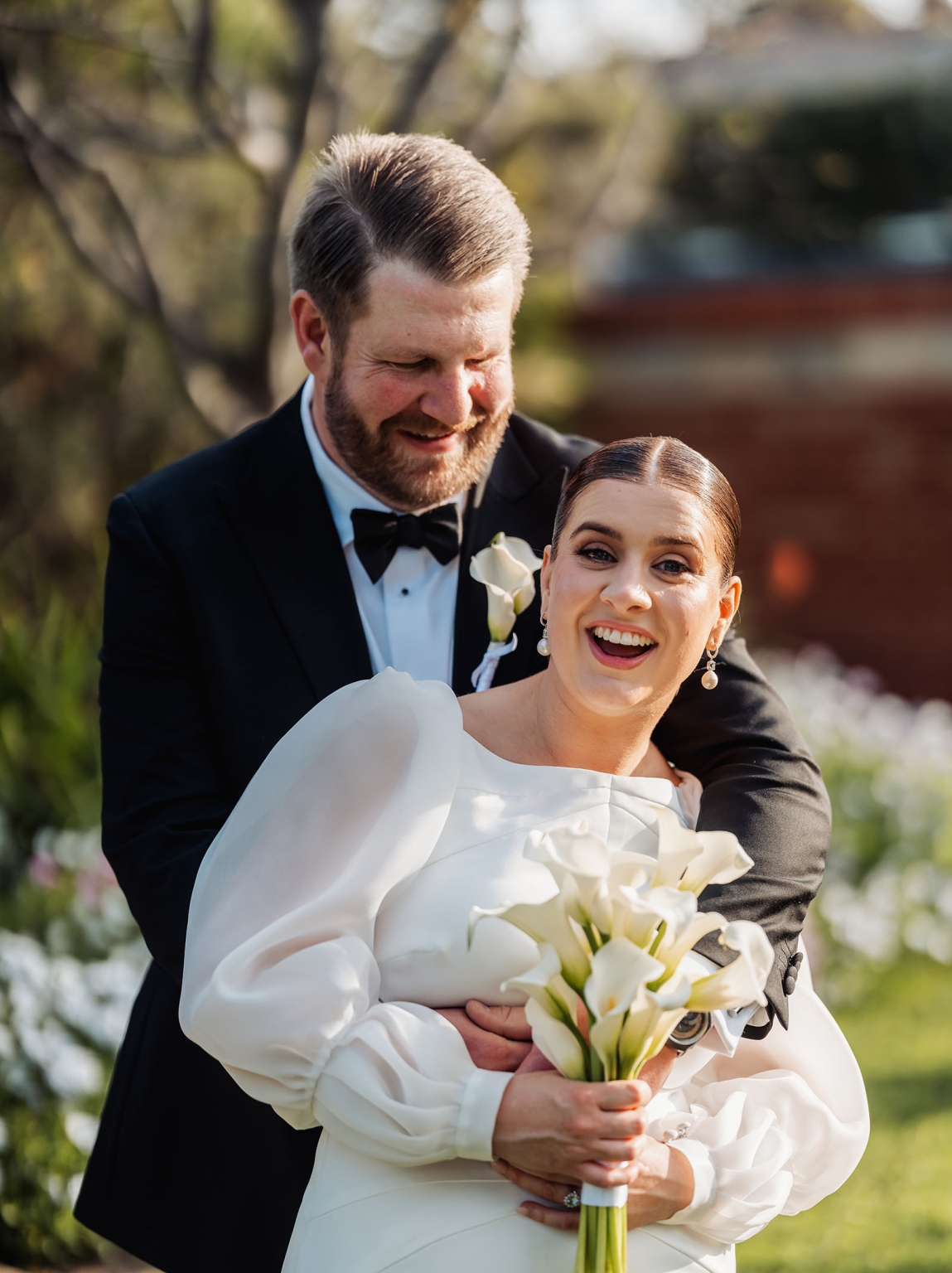 st joseph's chapel wedding – diana & michael 31 Diana smiling with a bouquet of white calla lilies as Michael embraces her from behind at their Sunnybrae wedding