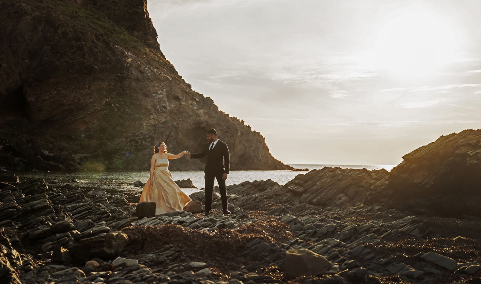 Ebony and Punit holding hands on a rocky beach beneath coastal cliffs at Second Valley