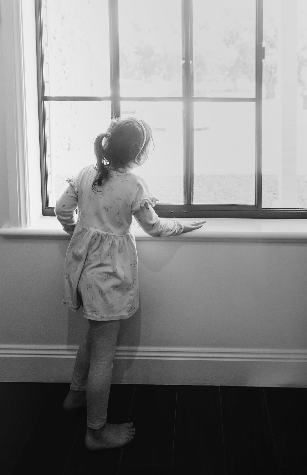 serafino winery wedding – maor & sasha 11 Young girl in a floral dress looking out an apartment window during wedding preparations